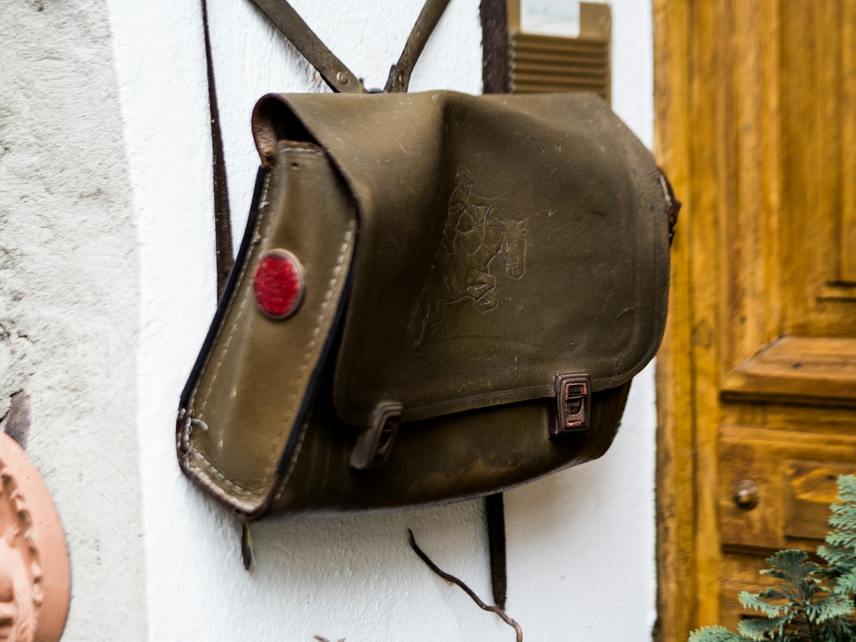Weathered olive leather satchel hanging against wood